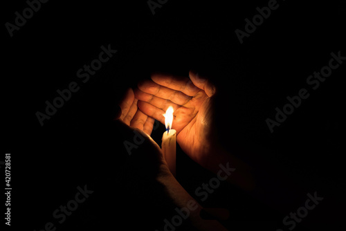 Two hands protecting candle light from the wind.