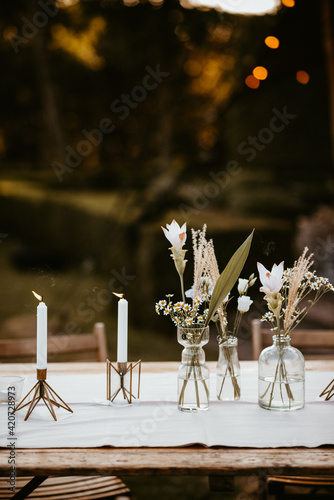 beautiful rustic styled table with linen, vases with dried flowers and candles lit in messing candle holders