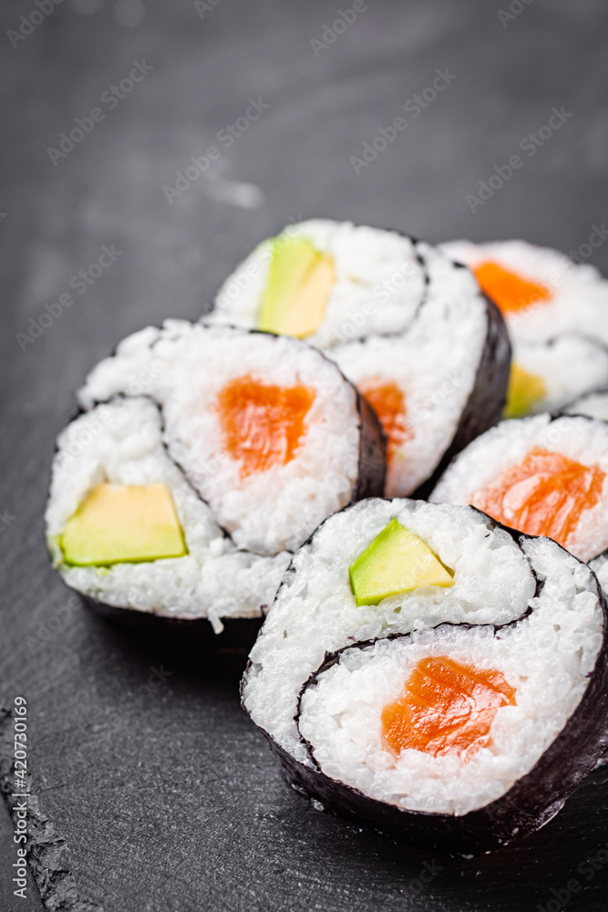 appetizing sushi roll futomaki yin yang with salmon and avocado on a black stone plate appetizing sushi roll futomaki yin yang with salmon and avocado on a black stone plate