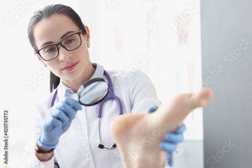 Woman podiatrist examining heel of patient using magnifying glass photo