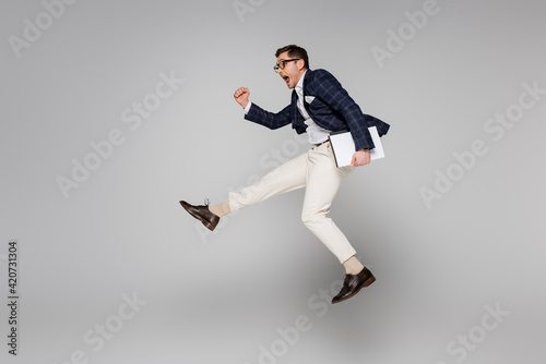 full length of amazed businessman holding paper folder while flying on grey