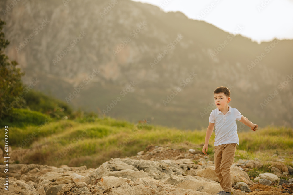 Boy plays and throws stones. Child with big mountains in the background. Holidays in the mountains with the family 