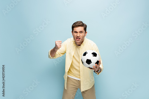 irritated man in yellow shirt holding football on blue