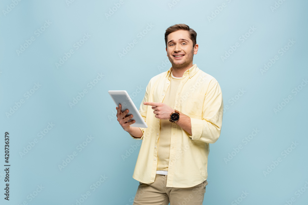 cheerful man in yellow shirt pointing with finger at digital tablet isolated on blue cheerful man in yellow shirt pointing with finger at digital tablet isolated on blue