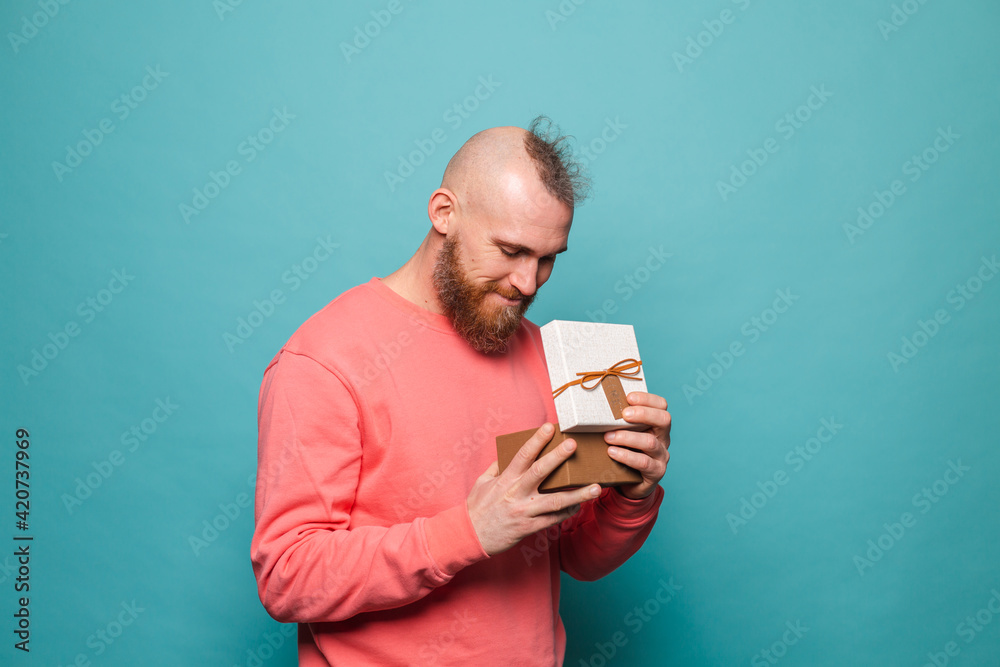 Bearded european man in casual peach isolated on turquoise background excited opening gift box Bearded european man in casual peach isolated on turquoise background excited opening gift box