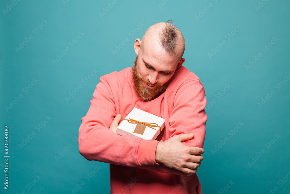 Bearded european man in casual peach isolated on turquoise background happy hugging gift box Bearded european man in casual peach isolated on turquoise background happy hugging gift box