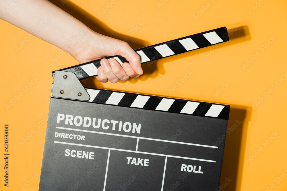 Obraz premium Hand holding film clapperboard on yellow studio background