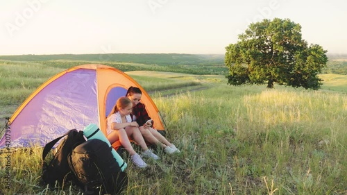 Family Enjoying Camping Holiday. Mother and daughter sitting in camping tent. Happy family camping in the park. Family weekend outdoor, local travel on nature, trekking, camp lifestyle.