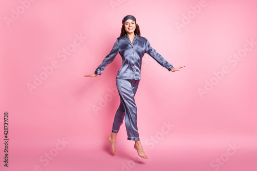 Full length body size photo of brunette wearing sleepwear jumping smiling isolated on pastel pink color background photo