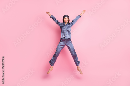 Full length body size photo of girl wearing blue nightwear jumping playful like star smiling isolated on pastel pink color background