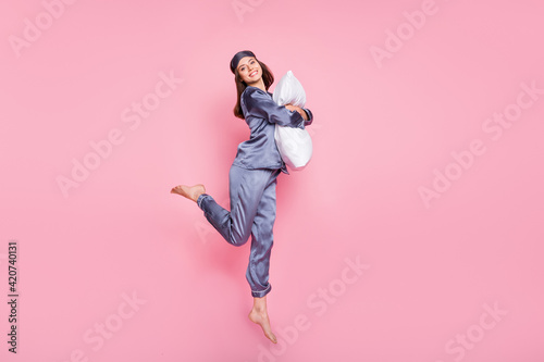 Full length body size photo of girl wearing pajama hugging embracing pillow jumping isolated on pastel pink color background