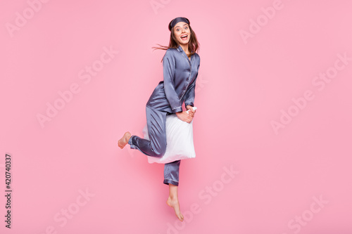 Full length body size photo of girl riding pillow on pajama party laughing in blue silk sleepwear isolated on pastel pink color background