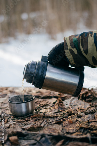 Man pours a hot tea from a thermos into a cup outdoors