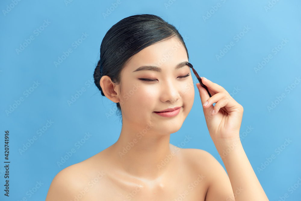 Beautiful young woman applying eyebrow brush on blue Beautiful young woman applying eyebrow brush on blue