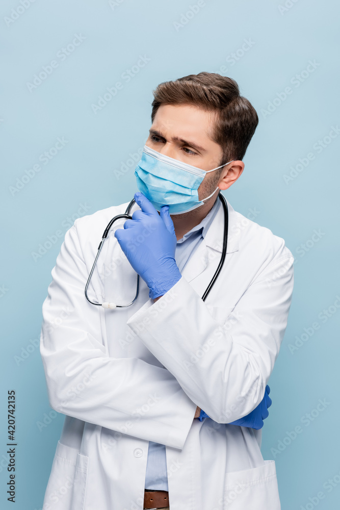 thoughtful doctor in medical mask and white coat with stethoscope isolated on blue thoughtful doctor in medical mask and white coat with stethoscope isolated on blue
