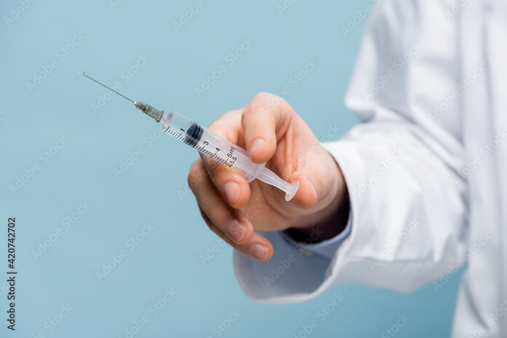 cropped view of doctor holding syringe in hand isolated on blue cropped view of doctor holding syringe in hand isolated on blue