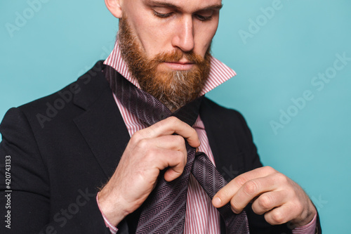 Фотография Bearded european businessman in dark suit isolated on turquoise background ties