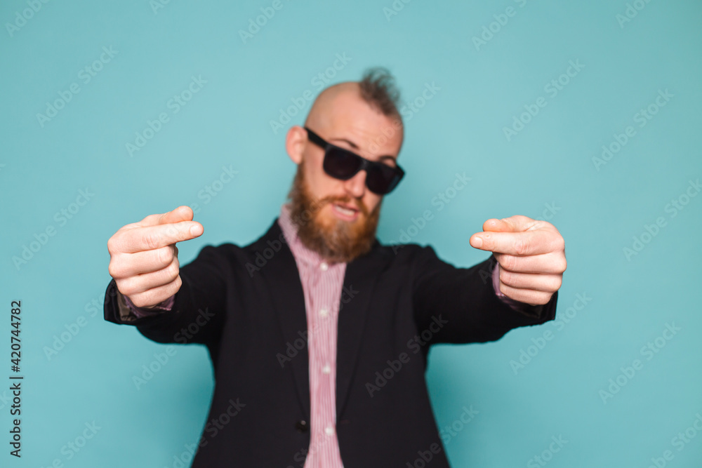 Naklejka premium Bearded european businessman in dark suit isolated on turquoise background shows money gesture, asking for help