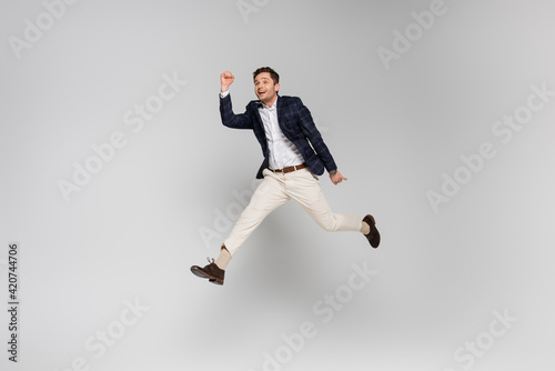 full length of cheerful young man with clenched fists levitating on grey
