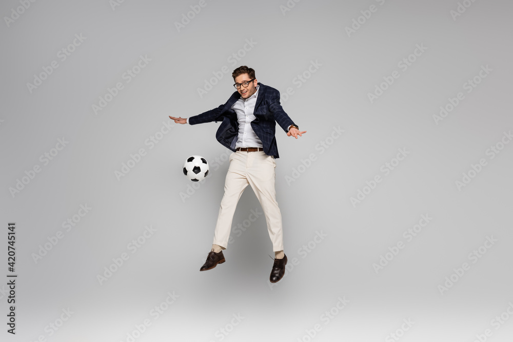 full length of smiling businessman playing football while levitating on grey