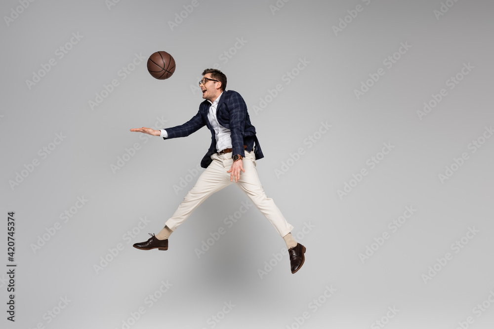 full length of happy businessman playing basketball while levitating on grey full length of happy businessman playing basketball while levitating on grey