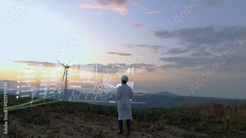 Adult man in white uniform working on wind farm on sunset using futuristic technology with 3d model construction of windmill buildings. Agronomy business. Tech innovation. Hi-tech concept.Human future
