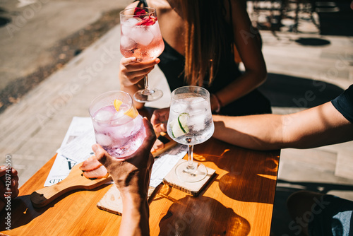 Group of friends sitting on the summer terrace holding cocktails and snacks on the table