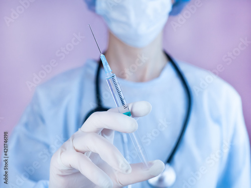 Female doctor or nurse in medical mask and in protective gloves holds a syringe with injection in hands. Influenza and coronavirus vaccination. Close-up.