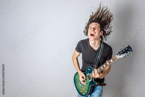 Young man is playing an electric guitar singing and waving his long hair. Emotional performance of rock and roll