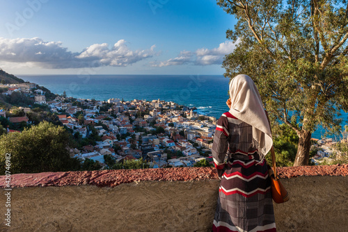Young muslim woman observig the view of the harbor city below with blue sky and sea in the background. photo