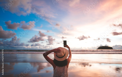 Rear view of adult woman relax in nature travel on beach sea using smart phone with sunset sky.