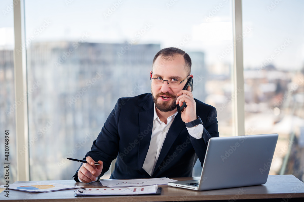 Adult male businessman, teacher, mentor looks at a laptop in his office. Office work. Development of a new business project Adult male businessman, teacher, mentor looks at a laptop in his office. Office work. Development of a new business project