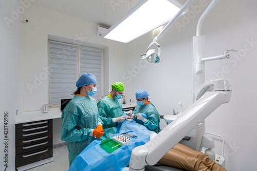 Team of dental surgeons performs surgery on teeth. in a modern clinic. Young dentist. Teamwork. Tooth doctor orthodontist surgeon doing medical operation on root canals. Stomatology office. 