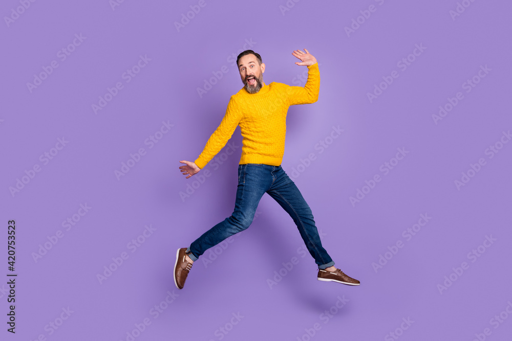 Photo of excited man jump run raise hands wear yellow pullover jeans footwear isolated violet background