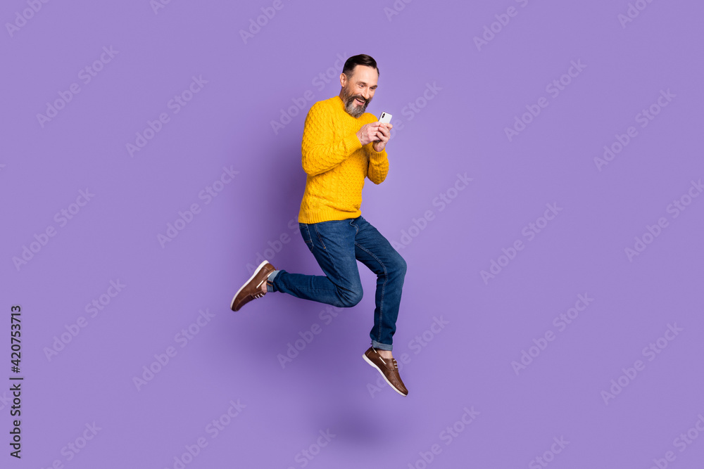 Photo of funny man jump run hold telephone look screen wear yellow pullover jeans shoes isolated purple background