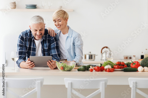 Happy senior couple use tablet, credit card, ordering food delivery in grocery in market doing shopping