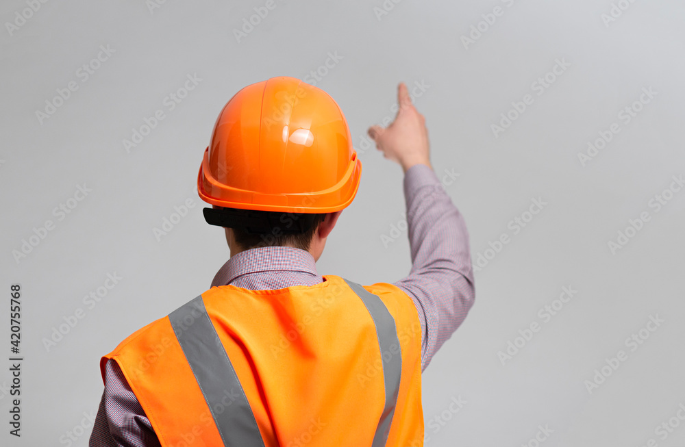 back of construction foreman in hard hat and reflective vest on grey studio background showing with finger direction forward