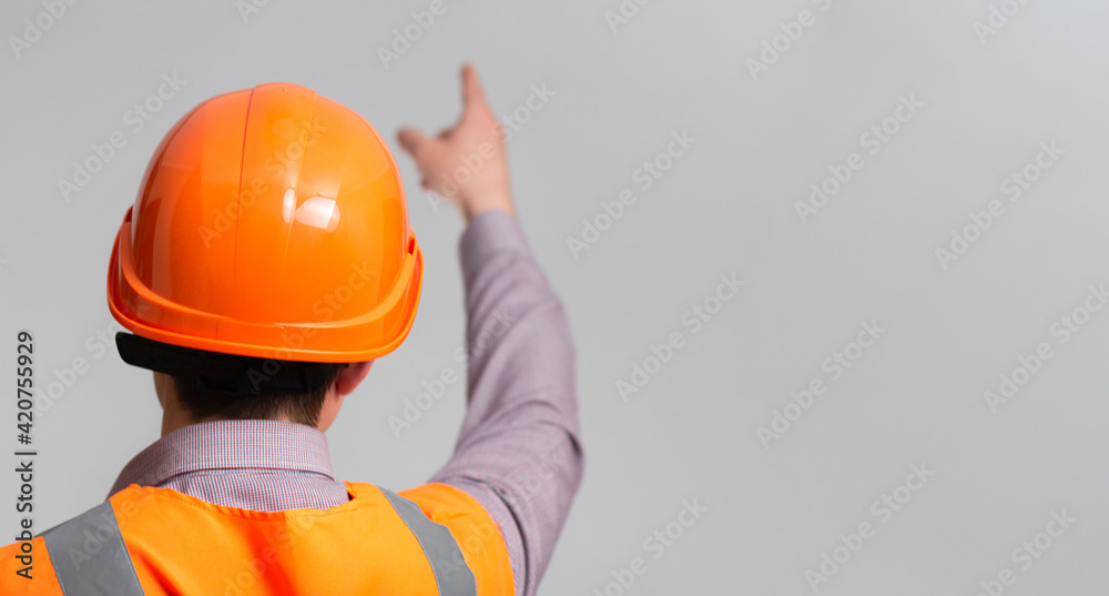 back of young construction worker in hard hat and reflective vest on grey studio background showing with hand direction forward back of young construction worker in hard hat and reflective vest on grey studio background showing with hand direction forward
