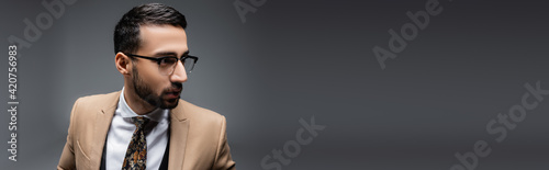 young arabian man in eyeglasses looking away on grey, banner