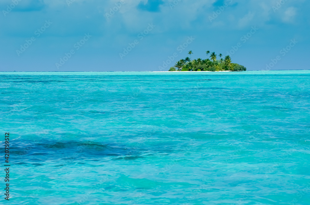 Uninhabited tropical island with palm trees. Cloudy sky and turquoise lagoon