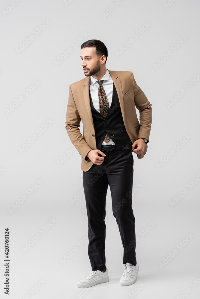 full length view of trendy arabian man in suit and sneakers posing on grey full length view of trendy arabian man in suit and sneakers posing on grey
