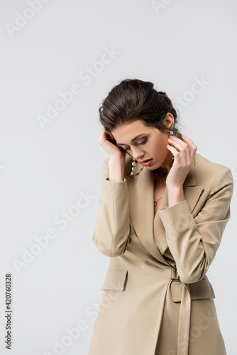 sensual, stylish woman touching face while posing with bowed head isolated on grey