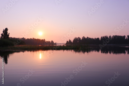 A colorful sunrise over the calm water surface of the lake. Summer landscape. Argazinskoe reservoir, Chelyabinsk, Russia