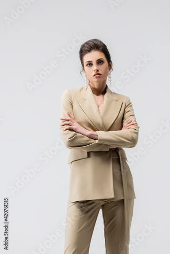 sensual woman in trendy pantsuit posing with crossed arms isolated on grey