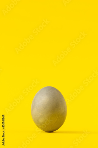 Uneavenly coloured gray easter egg on vivid yellow background. Minimal composition with copy space.