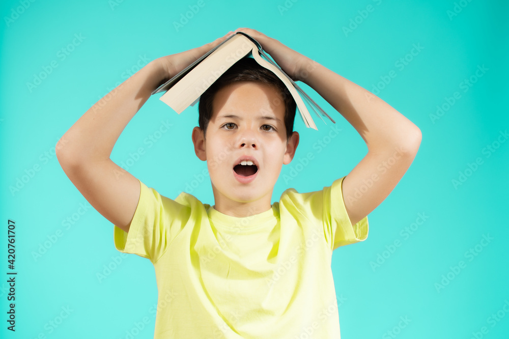 Portrait of surprised kid holding book above head, stand isolated over green background studio. Funny education concept Portrait of surprised kid holding book above head, stand isolated over green background studio. Funny education concept