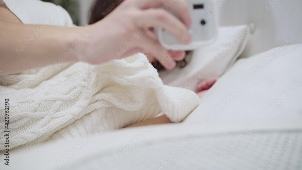 Close-up of sleeping Caucasian man waking up, turning off alarm clock, and hiding under white blanket. Portrait of sleepy young brunette guy in bed in the morning. Tiredness and resting concept. Close-up of sleeping Caucasian man waking up, turning off alarm clock, and hiding under white blanket. Portrait of sleepy young brunette guy in bed in the morning. Tiredness and resting concept.
