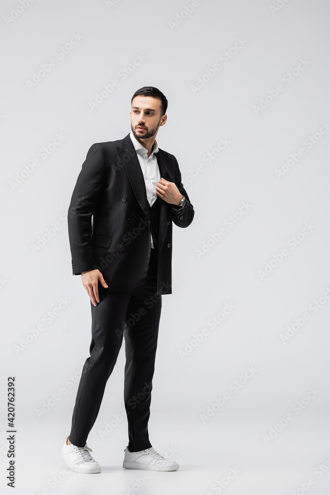 full length view of trendy arabian man looking away while posing on grey full length view of trendy arabian man looking away while posing on grey