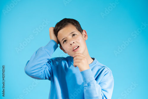 Young boy pensive isolated with blue sweater over blue background