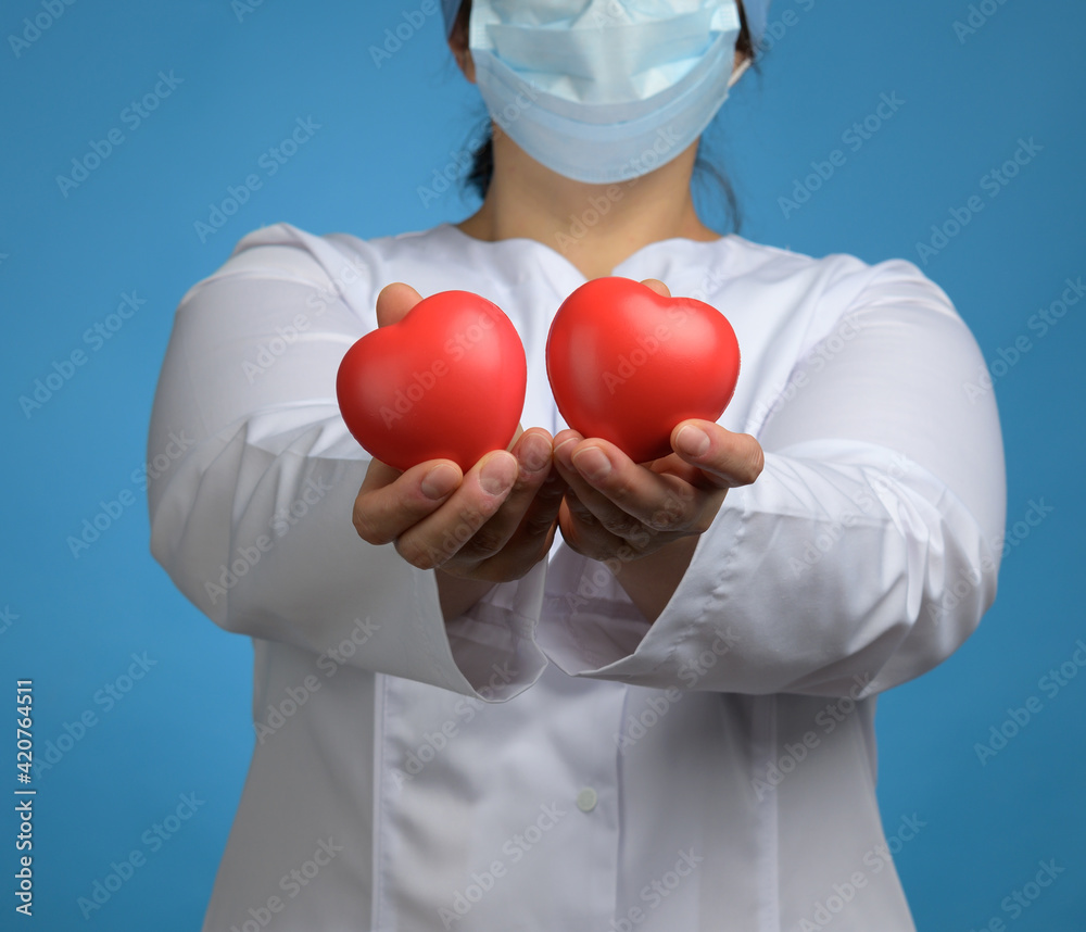 medic in a white coat, a mask stands and holds a red heart on a blue background medic in a white coat, a mask stands and holds a red heart on a blue background